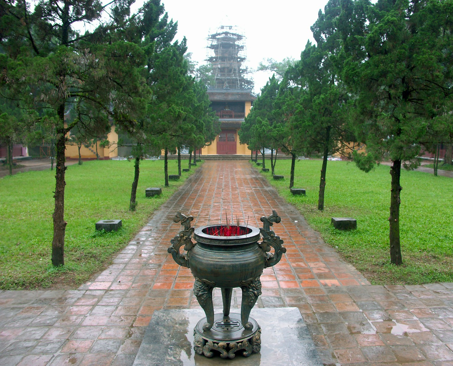 Scenic view of a garden with green trees featuring an incense burner and an ancient tower