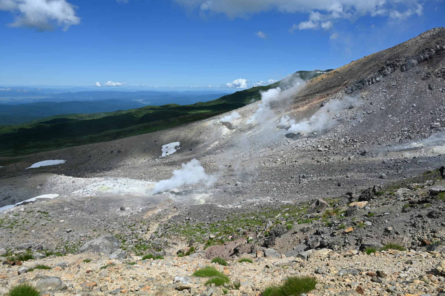 Vulkanische Hanglandschaft mit blauem Himmel und Wolken, die aufsteigende Dampfwolken zeigen