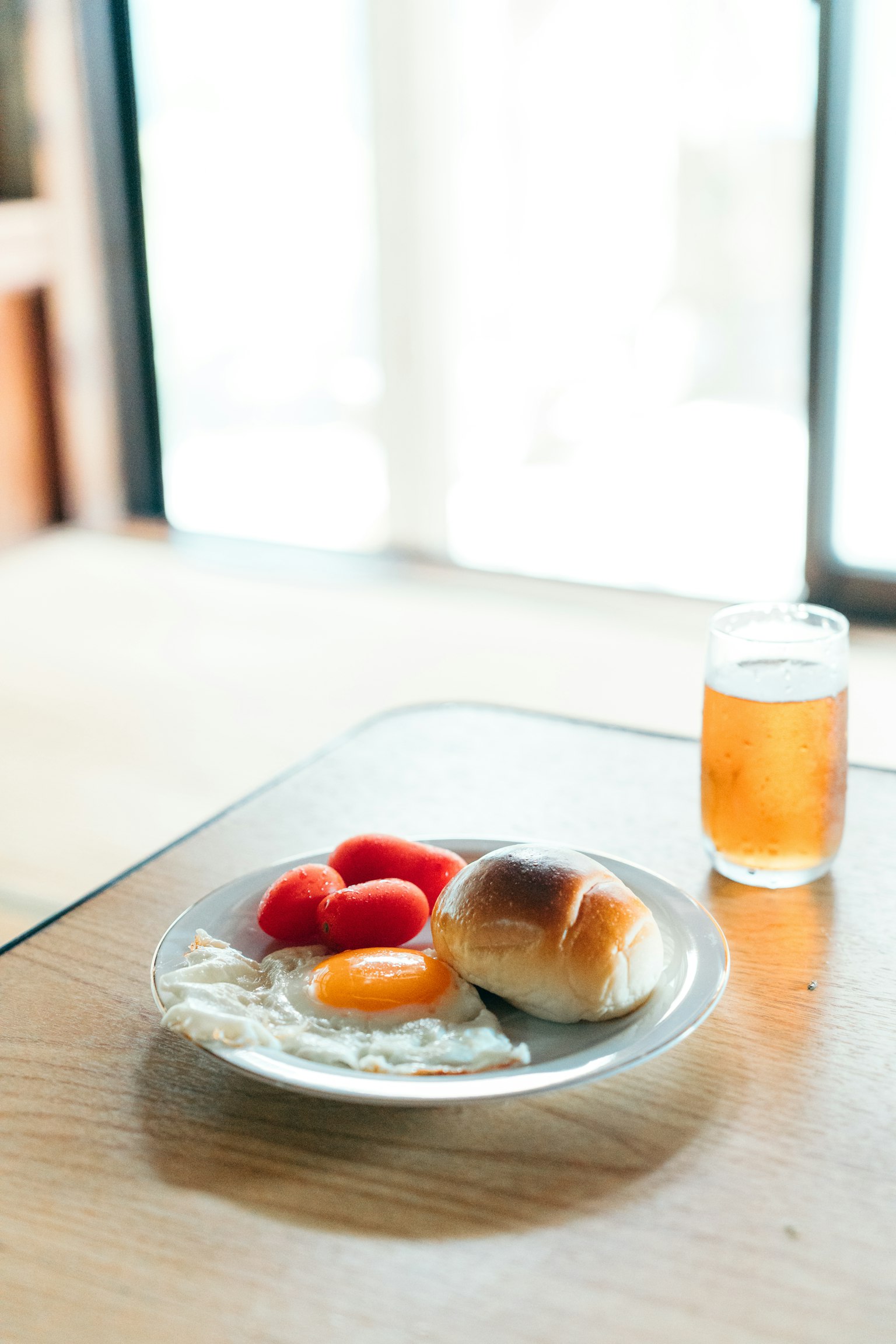 テーブルの上にある朝食プレートには目玉焼き、トマト、パン、飲み物が置かれている