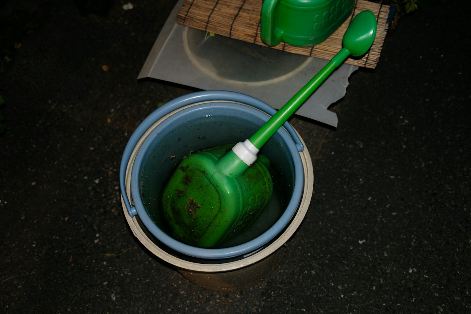 Arrosoir vert placé à l'intérieur d'un seau bleu la nuit