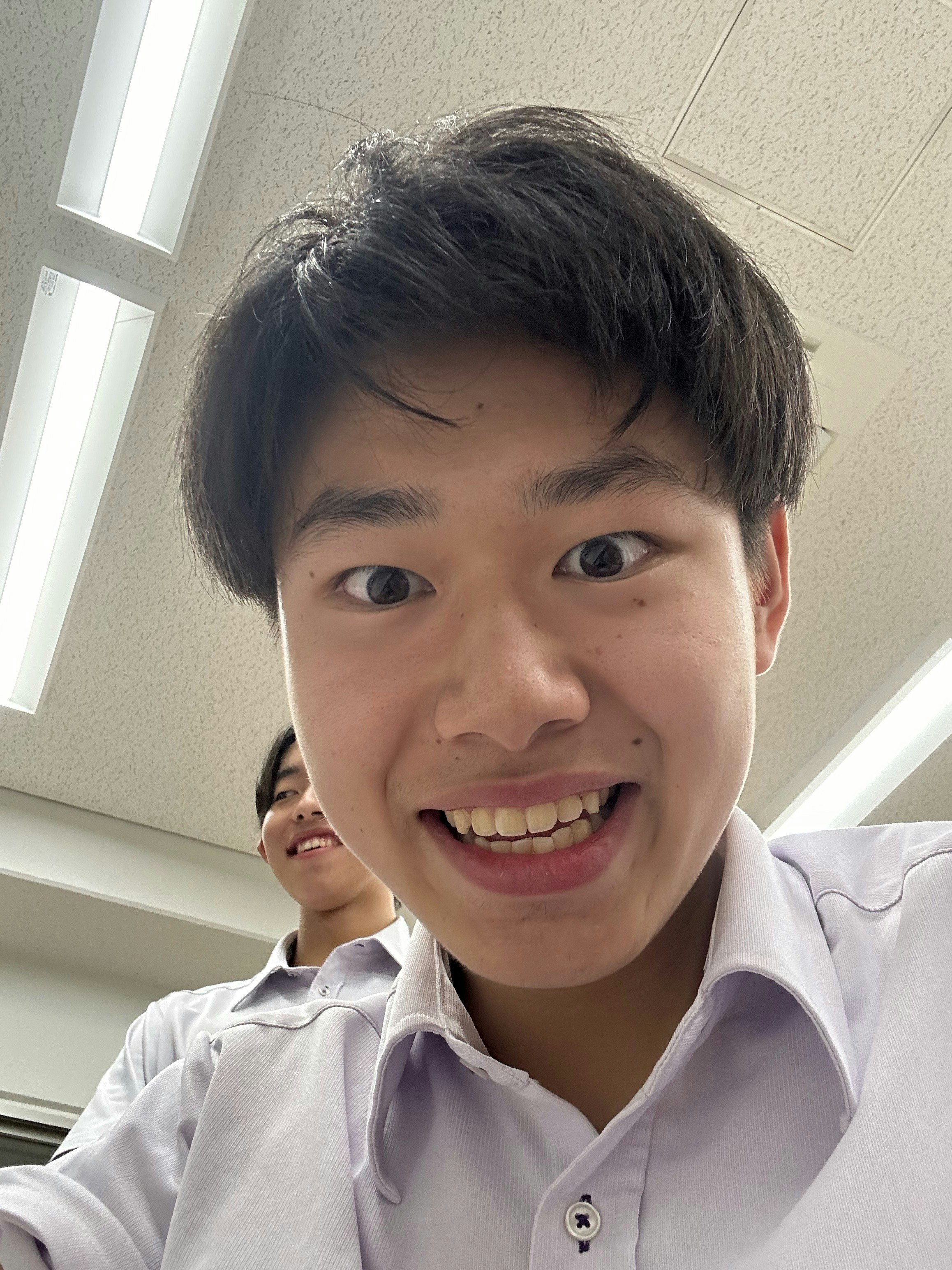白いシャツの男子学生が教室で笑顔の自撮り風画像