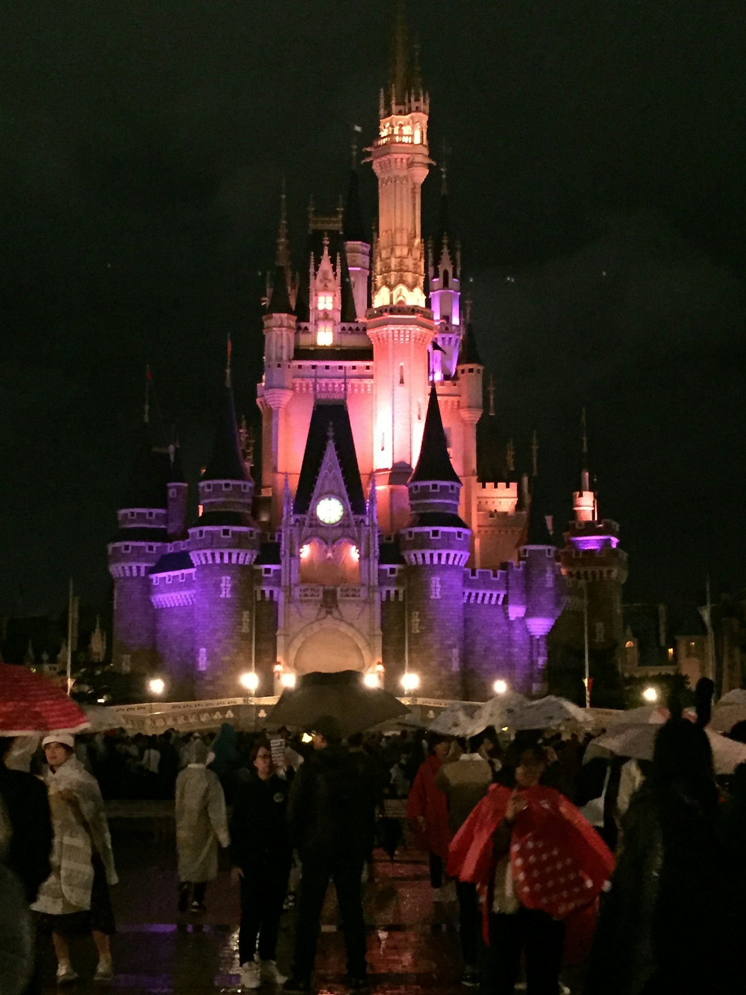 Castillo de la Cenicienta en Disneyland iluminado con luces moradas y naranjas por la noche