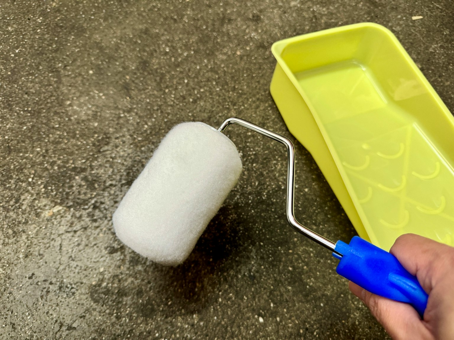 Rullo di vernice bianco e vassoio giallo su pavimento in cemento