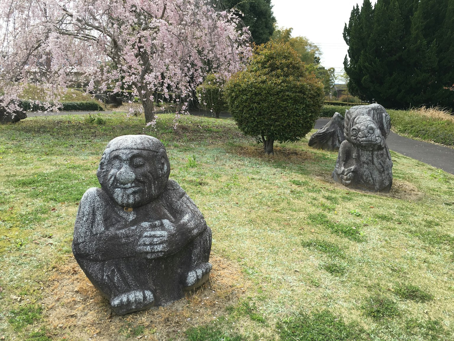 Deux statues en pierre dans un parc avec un cerisier