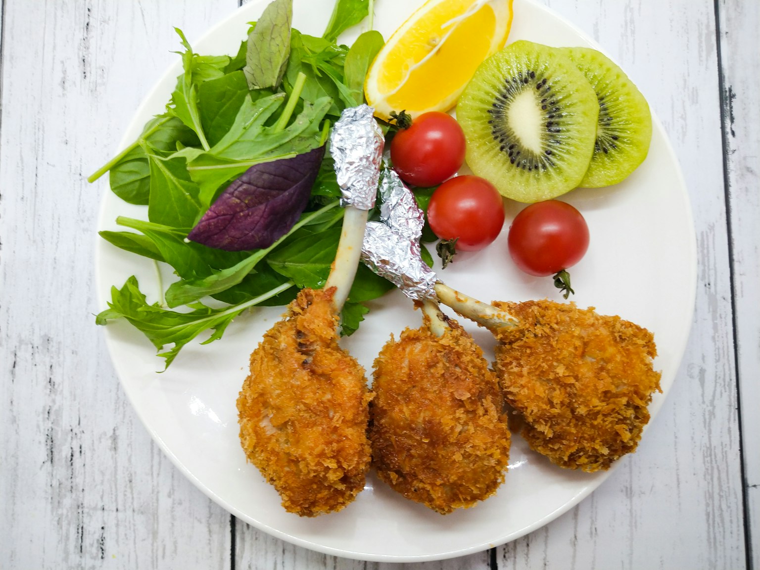 Drei frittierte Hähnchenschenkel auf einem Teller mit Salat und Früchten