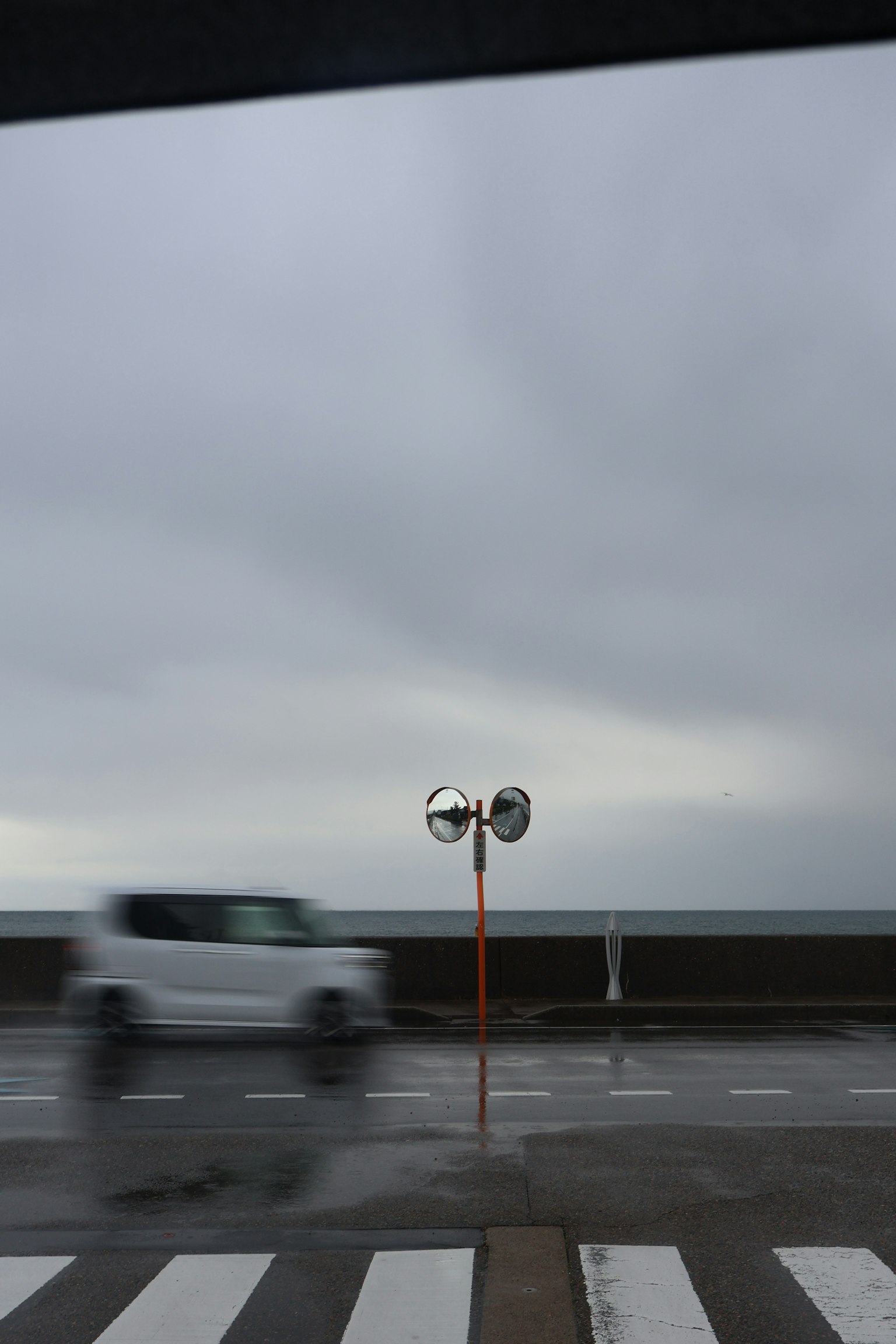 海の近くの道路にあるミラーと曇り空の風景