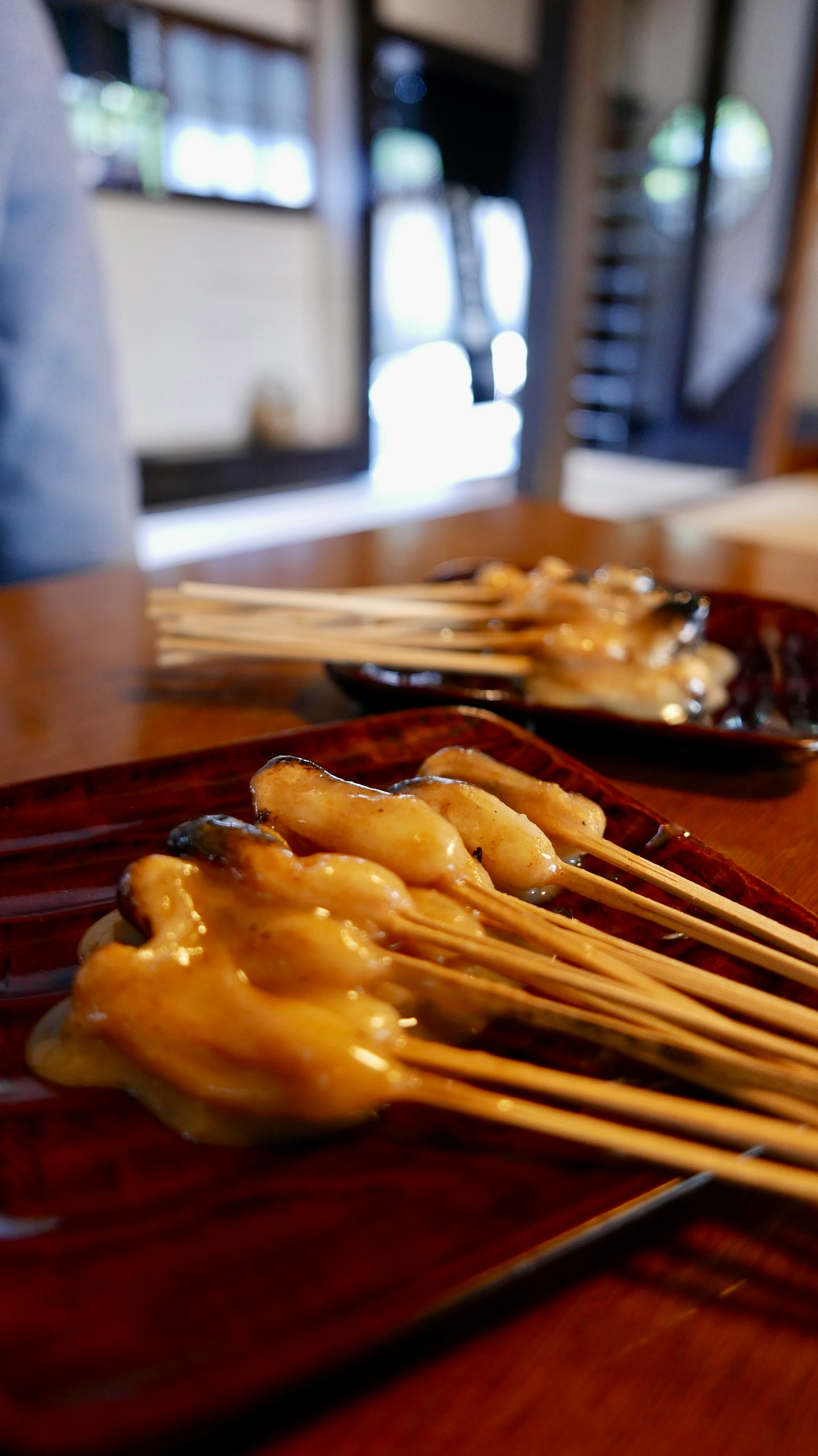 Gambar hidangan tusuk sate disajikan di atas piring dengan latar belakang interior Jepang tradisional