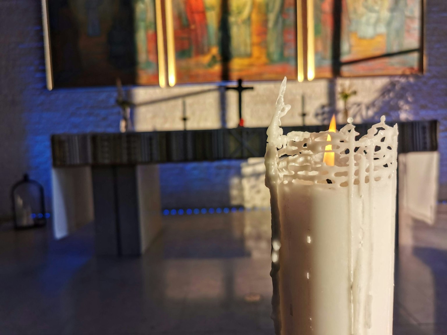 Una vela blanca encendida en el interior sereno de una iglesia con arte colorido de fondo