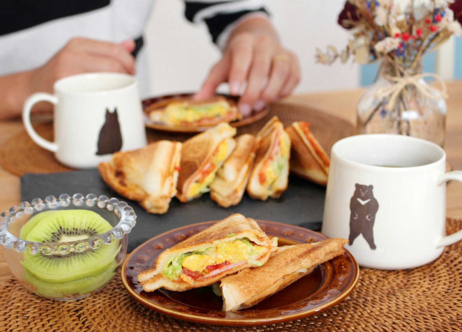 Una mesa con sándwiches y bebidas Un postre de fruta verde en primer plano Dos tazas con ilustraciones de osos