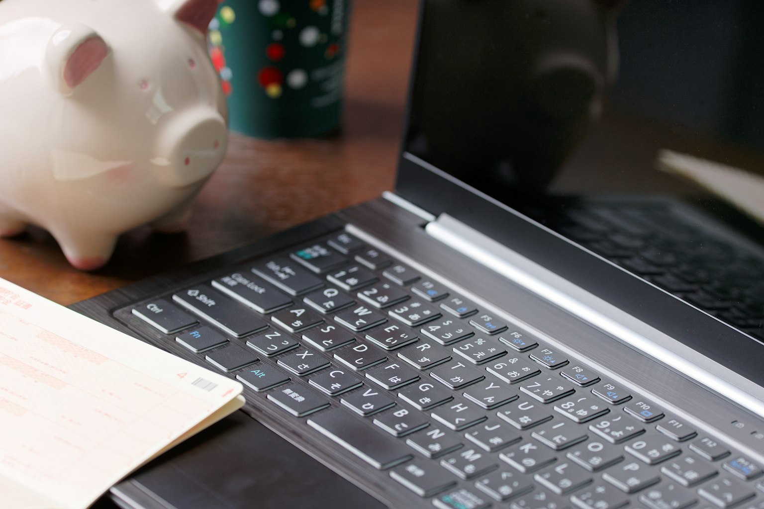Ordinateur portable sur un bureau avec une tirelire en forme de cochon rose et une tasse colorée