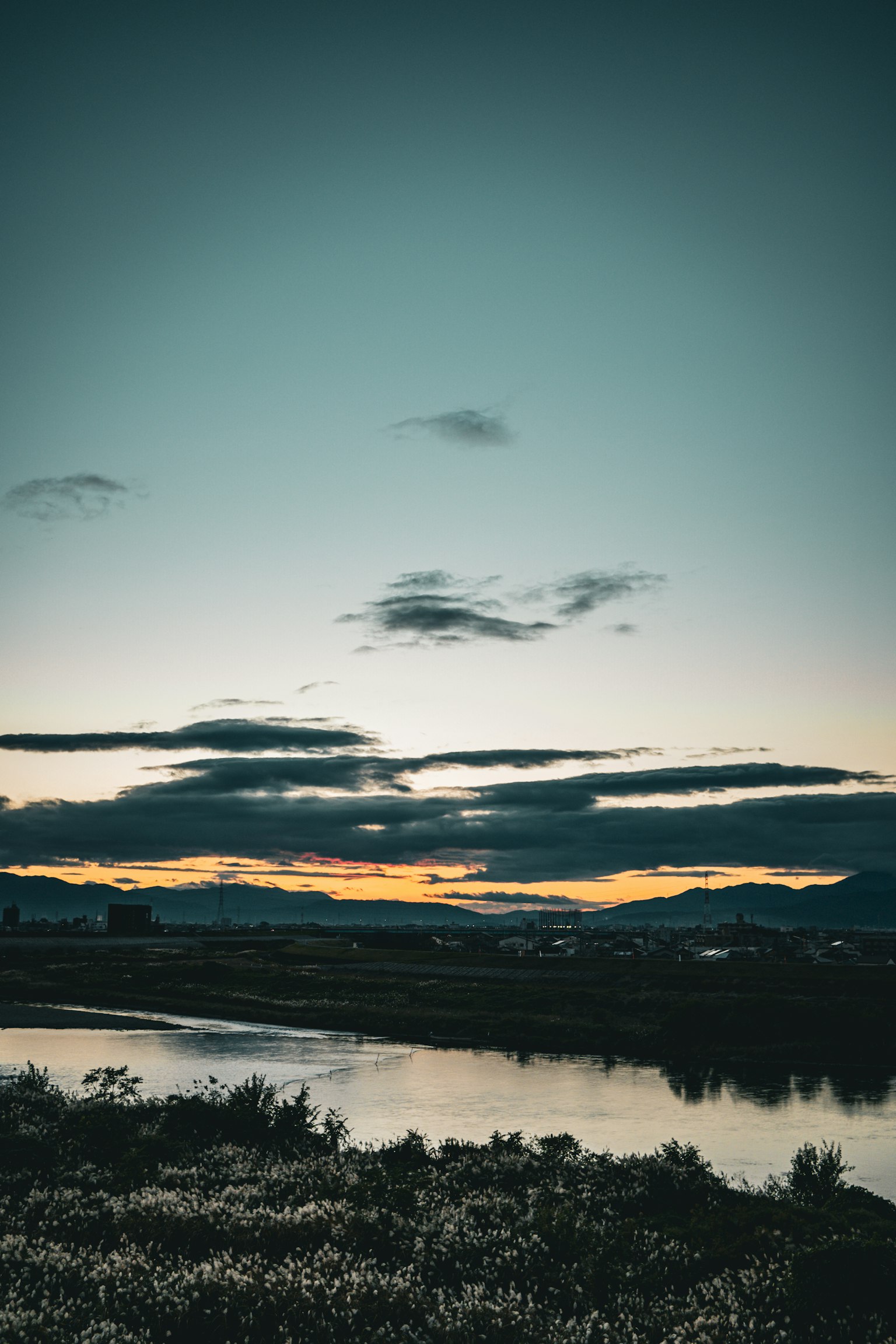 Paisaje de atardecer tranquilo con nubes y siluetas de montañas reflejadas en el agua