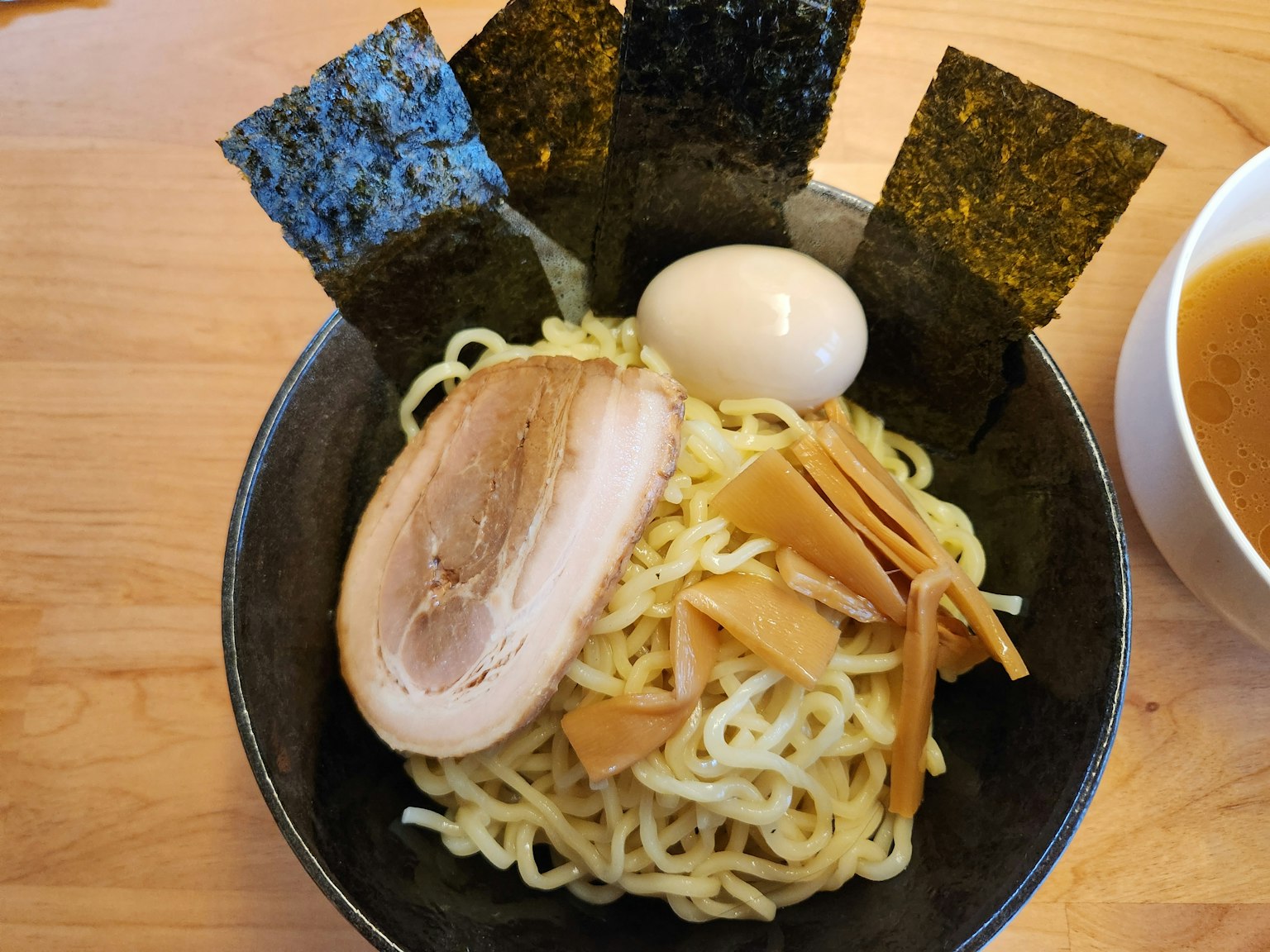Plat de tsukemen servi dans un bol noir avec des garnitures y compris chashu, œuf mollet, menma et algues