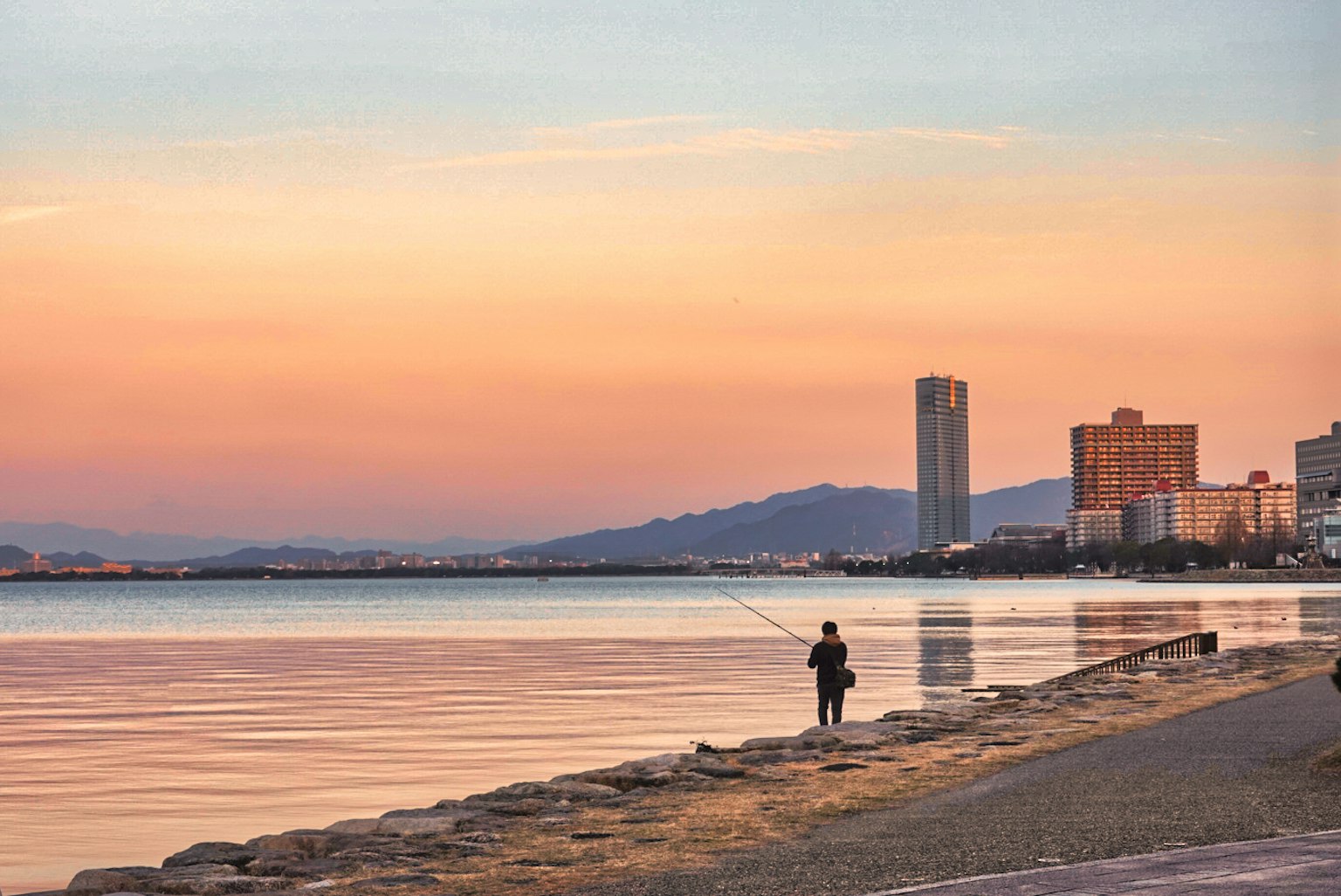 A person walking along the beach at sunset with city skyline