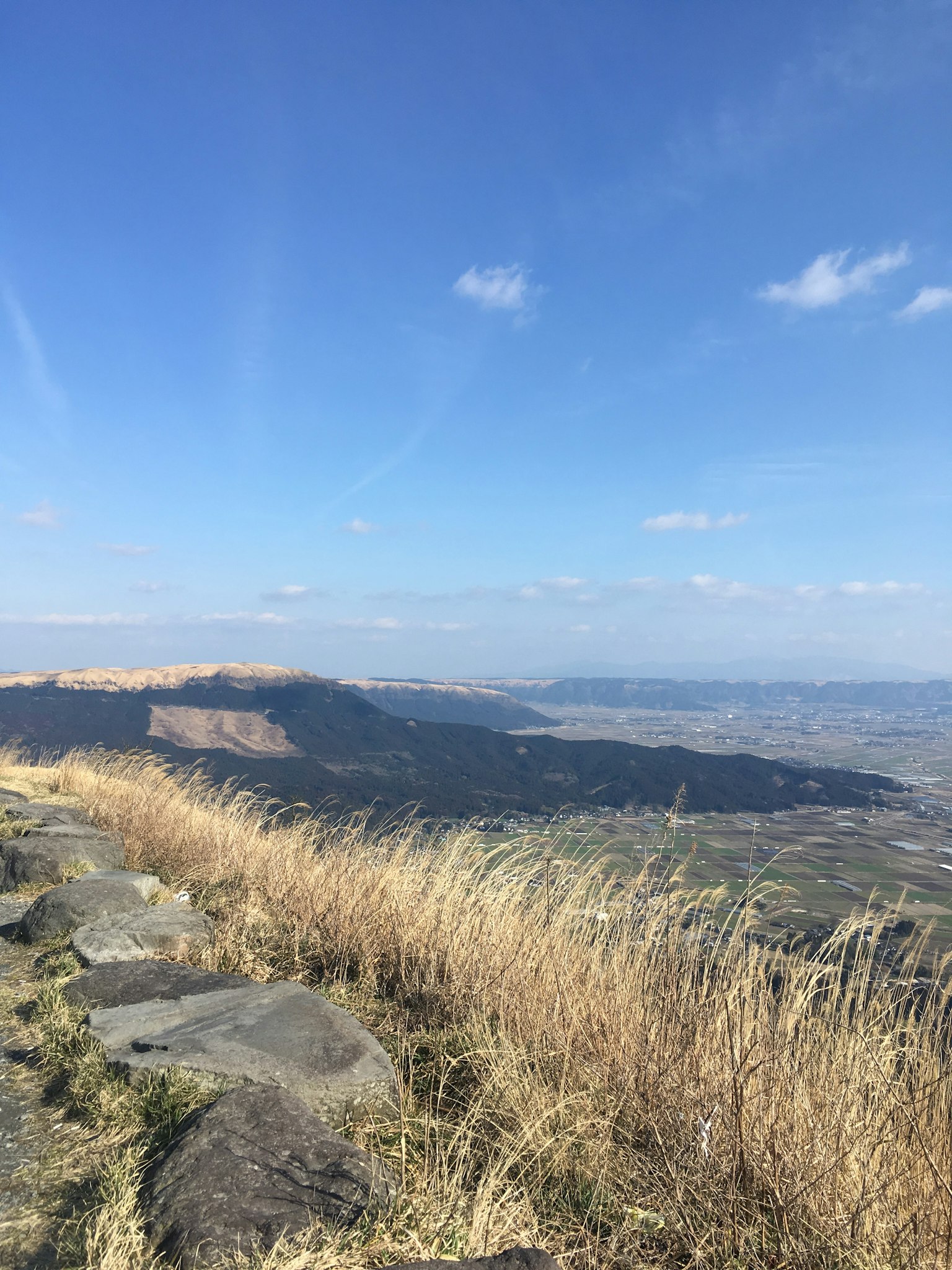 Vue expansive de collines herbeuses et de montagnes lointaines sous un ciel bleu