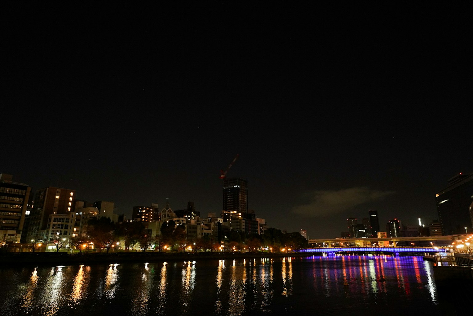 夜间城市景观在河中倒影，摩天大楼和五彩斑斓的桥灯