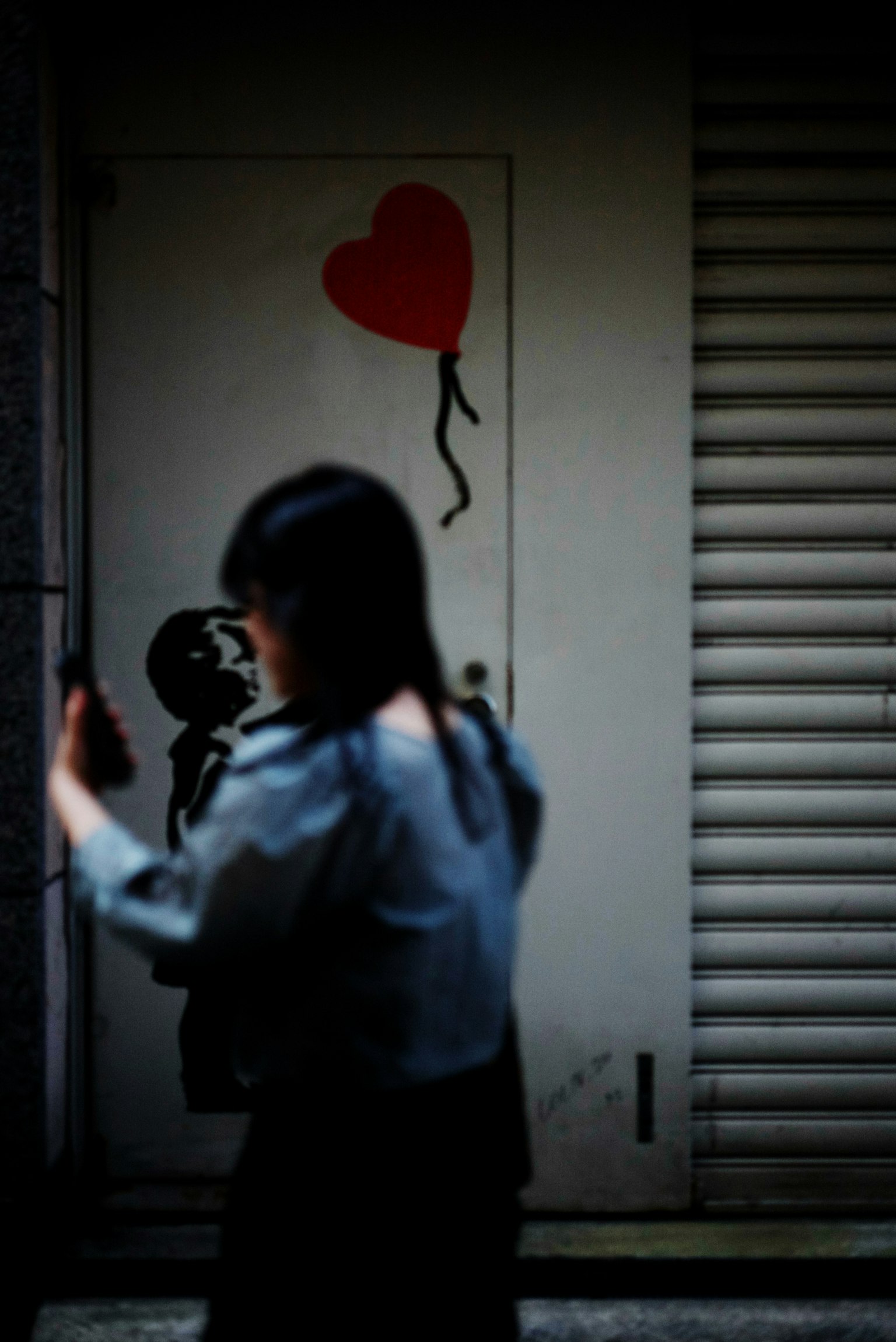 A woman walking with a smartphone in front of a door featuring a red heart balloon illustration