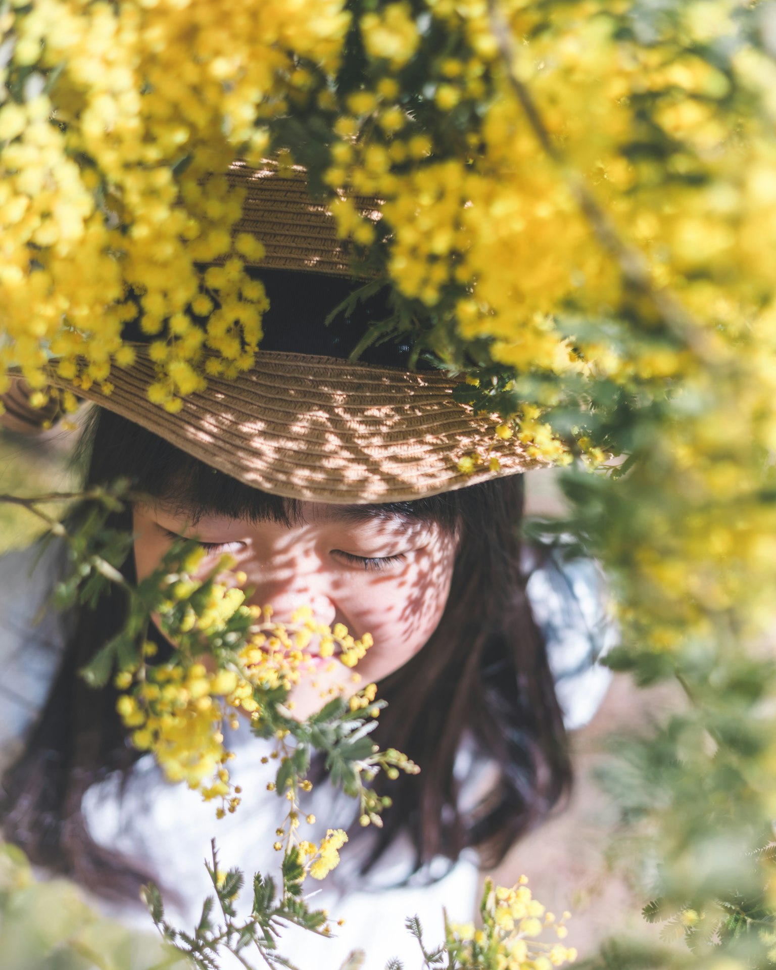 Una mujer asomándose entre flores amarillas con un sombrero de paja