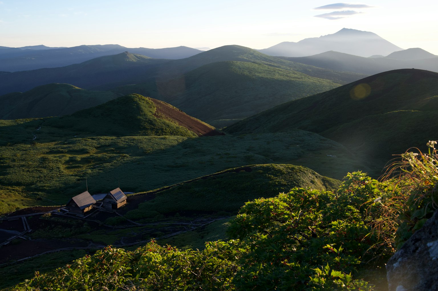 Paysage pittoresque avec des collines verdoyantes et des montagnes lointaines avec une petite maison