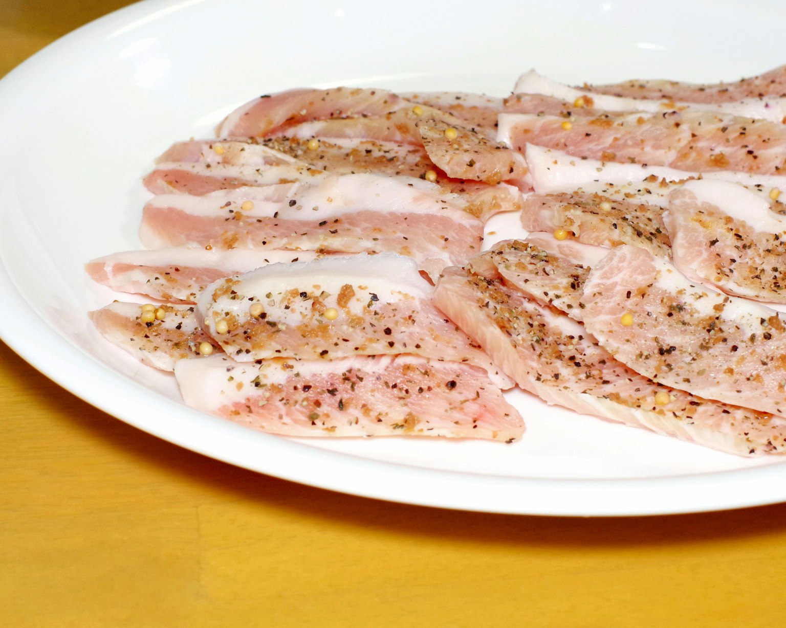 Daging tipis yang dibumbui disusun di atas piring putih