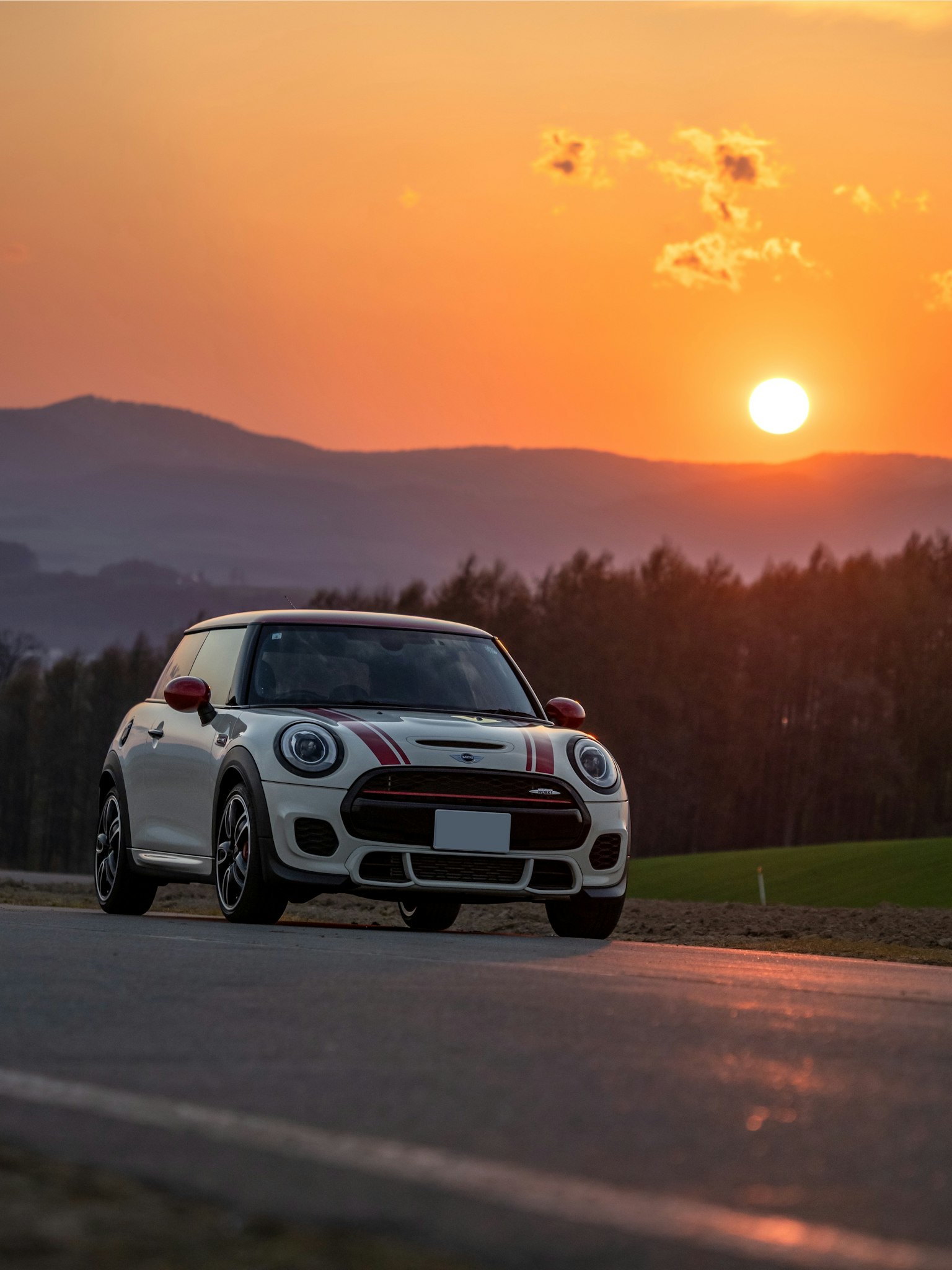 Una Mini Cooper bianca che guida su una strada con un tramonto sullo sfondo