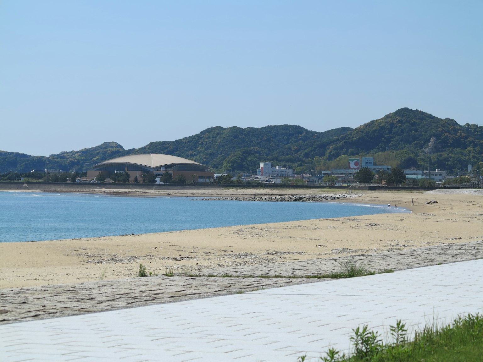 ทิวทัศน์ของทะเลสีน้ำเงินและชายหาดทราย มีภูเขาอยู่ด้านหลัง