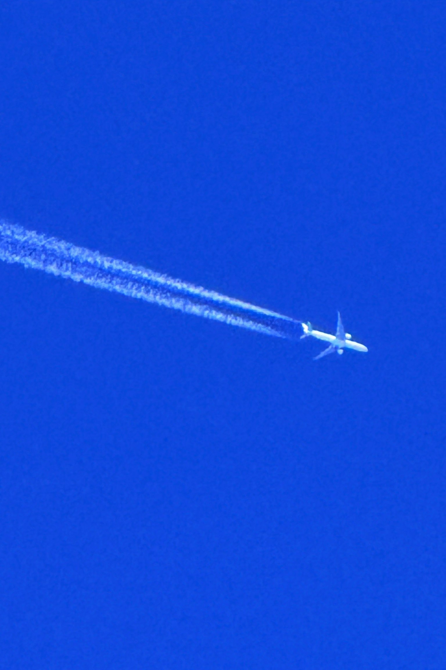 Ein Flugzeug fliegt in einem klaren blauen Himmel und hinterlässt eine Kondensstreifen