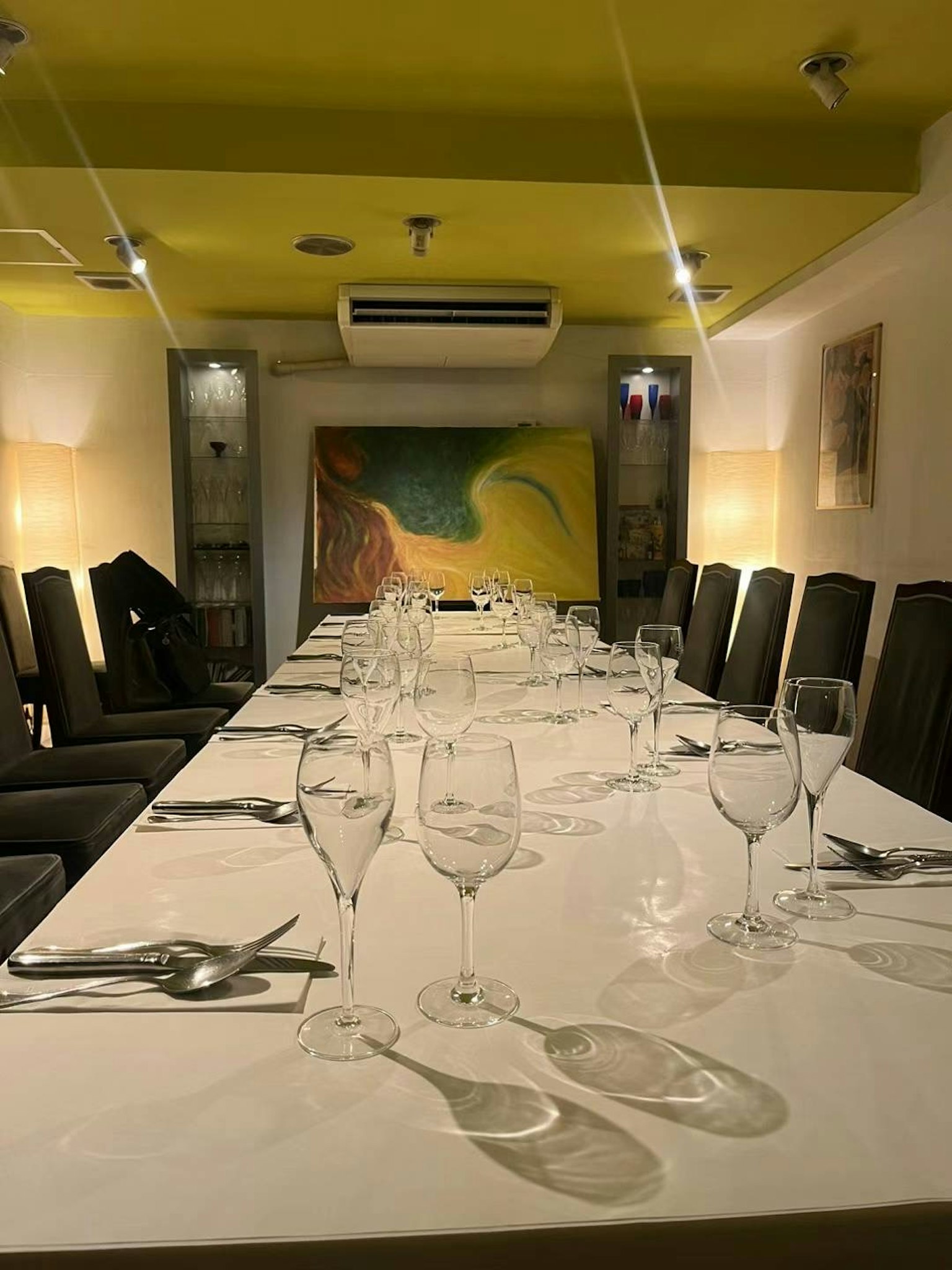餐厅内长桌上摆放着杯子和餐具，明亮的黄色天花板