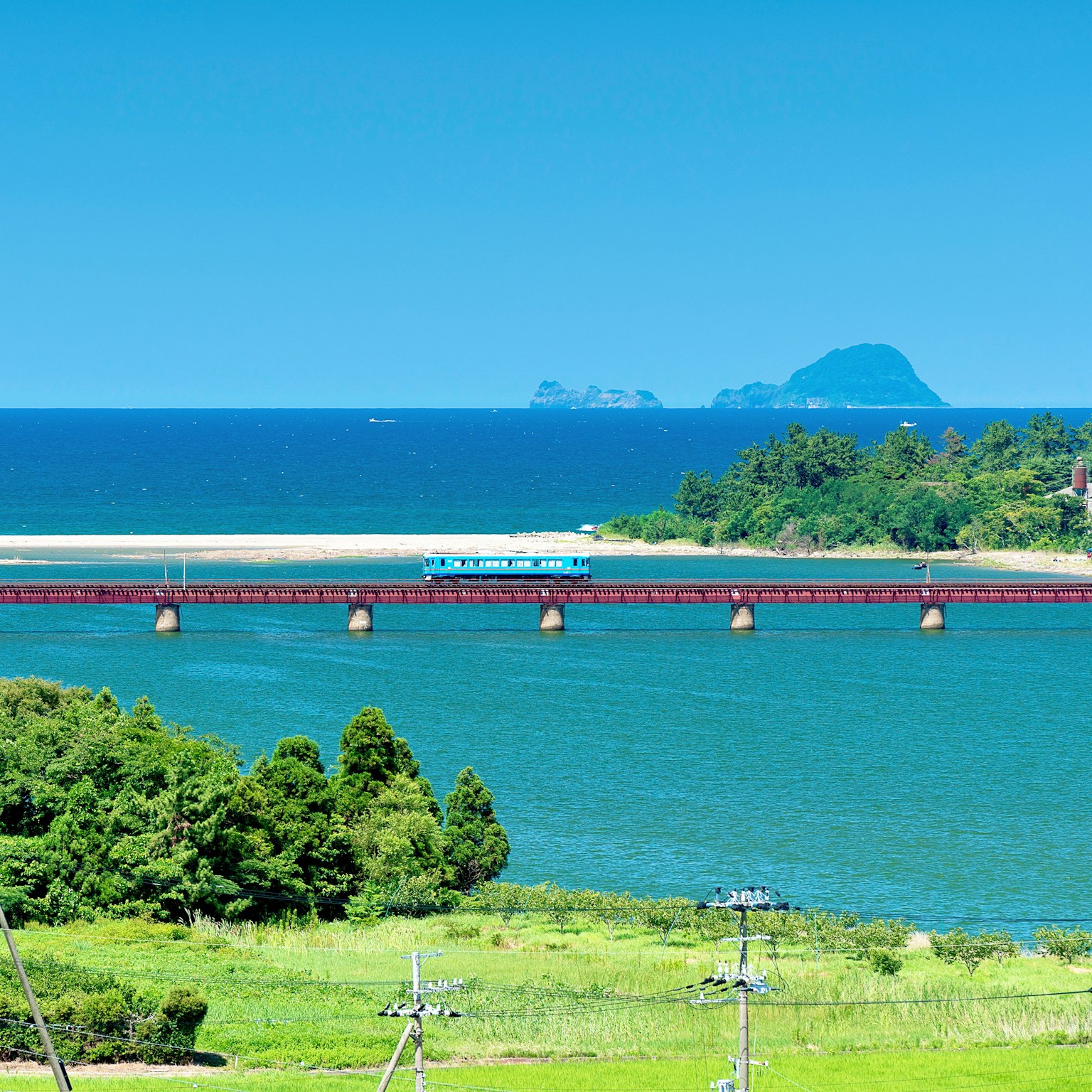 Pont ferroviaire avec un train bleu sur une eau turquoise et une verdure luxuriante