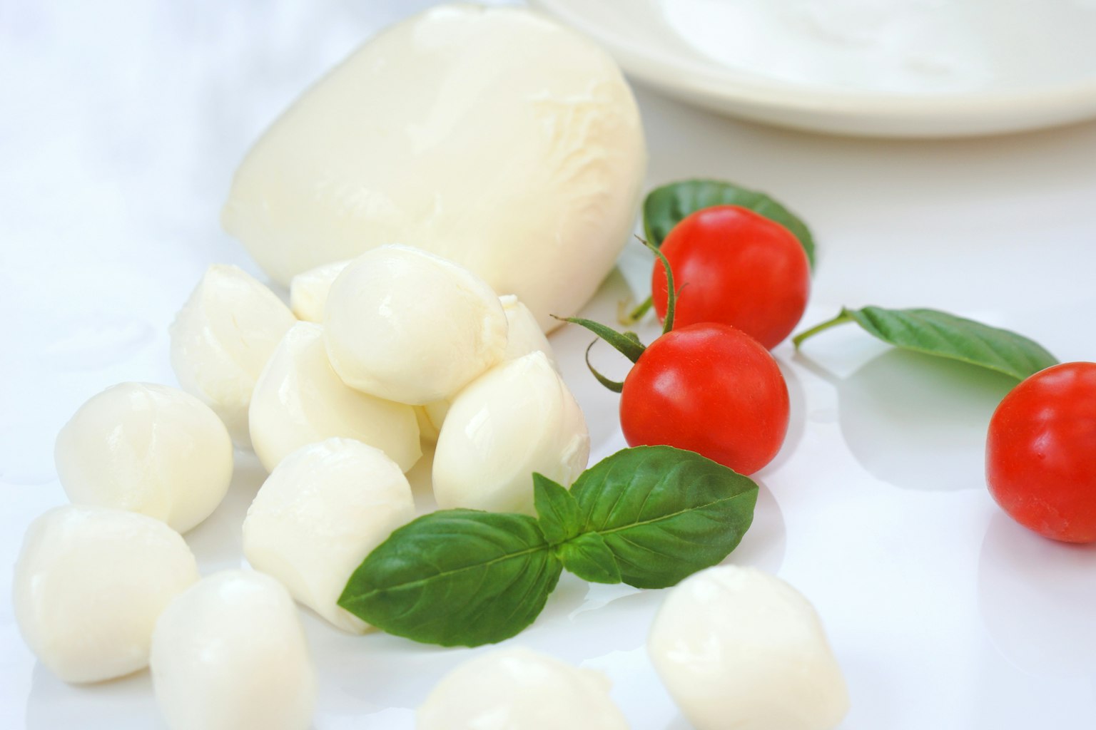 Frischer Mozzarella-Käse mit Kirschtomaten und Basilikumblättern auf einer weißen Oberfläche angeordnet
