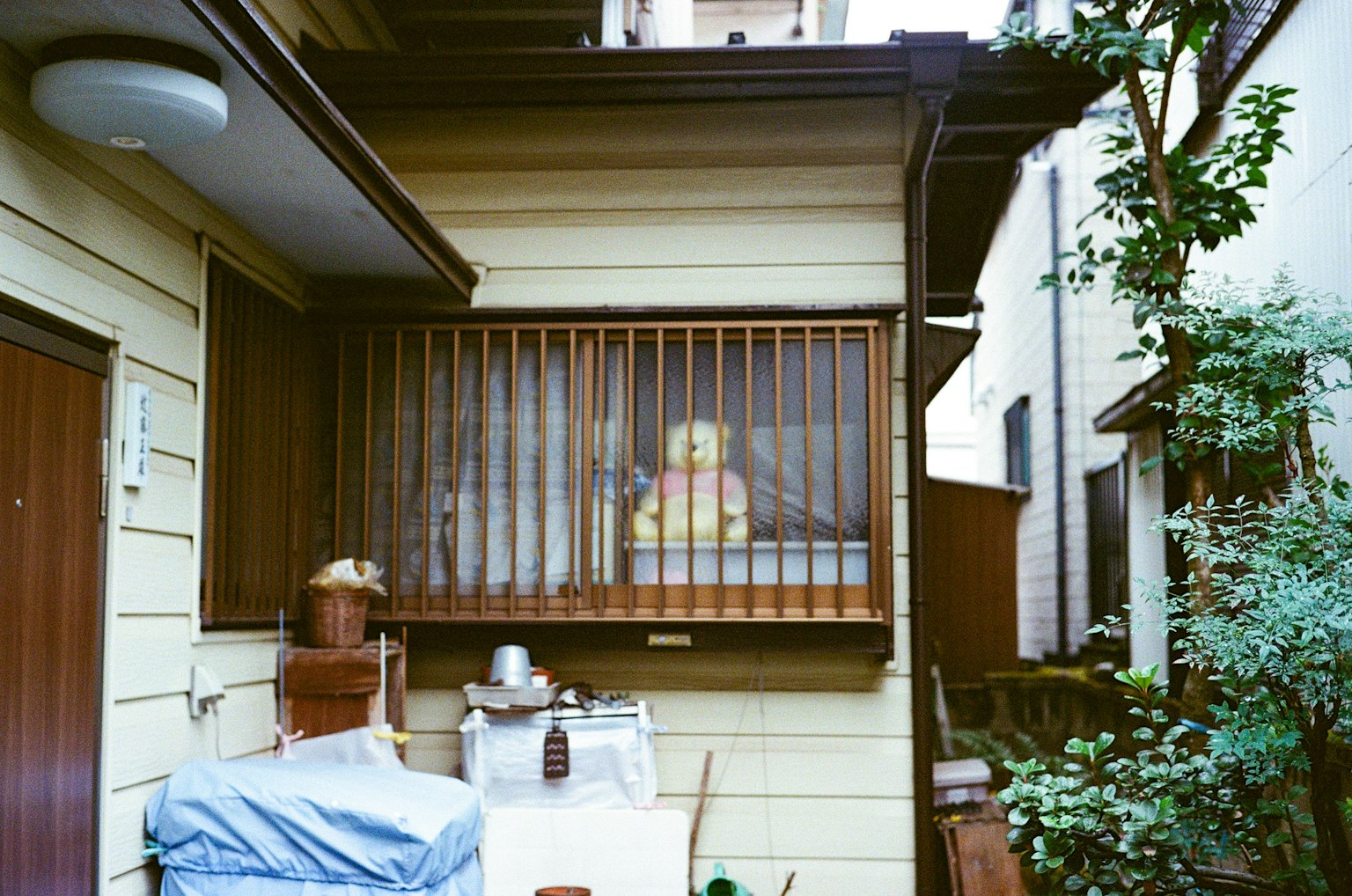 Extérieur d'une maison japonaise avec une poupée jaune visible à travers des barreaux de fenêtre