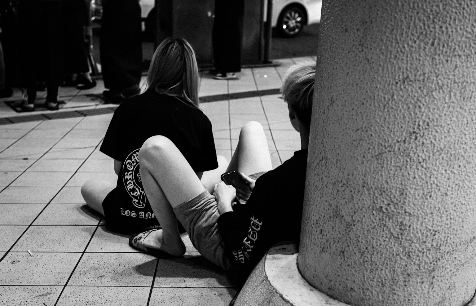 Two young people sitting near a pillar in a black and white photo