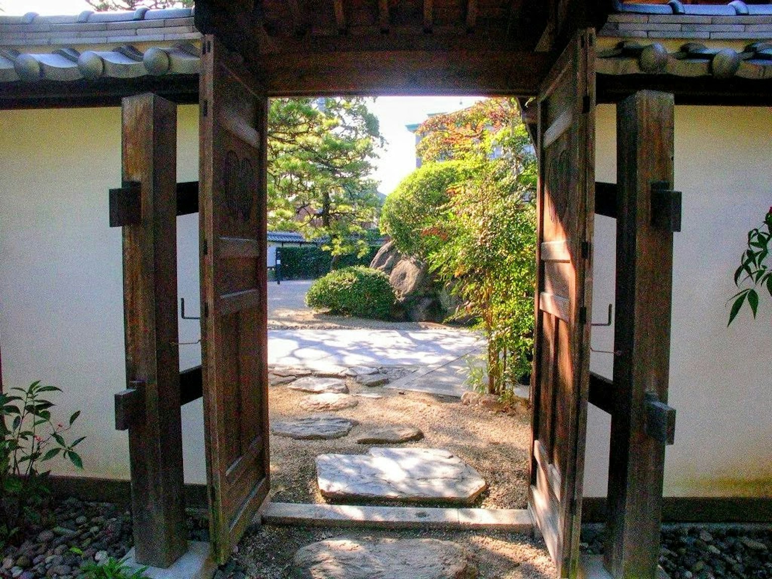 View of a Japanese garden through a wooden gate featuring lush greenery and stone pathway