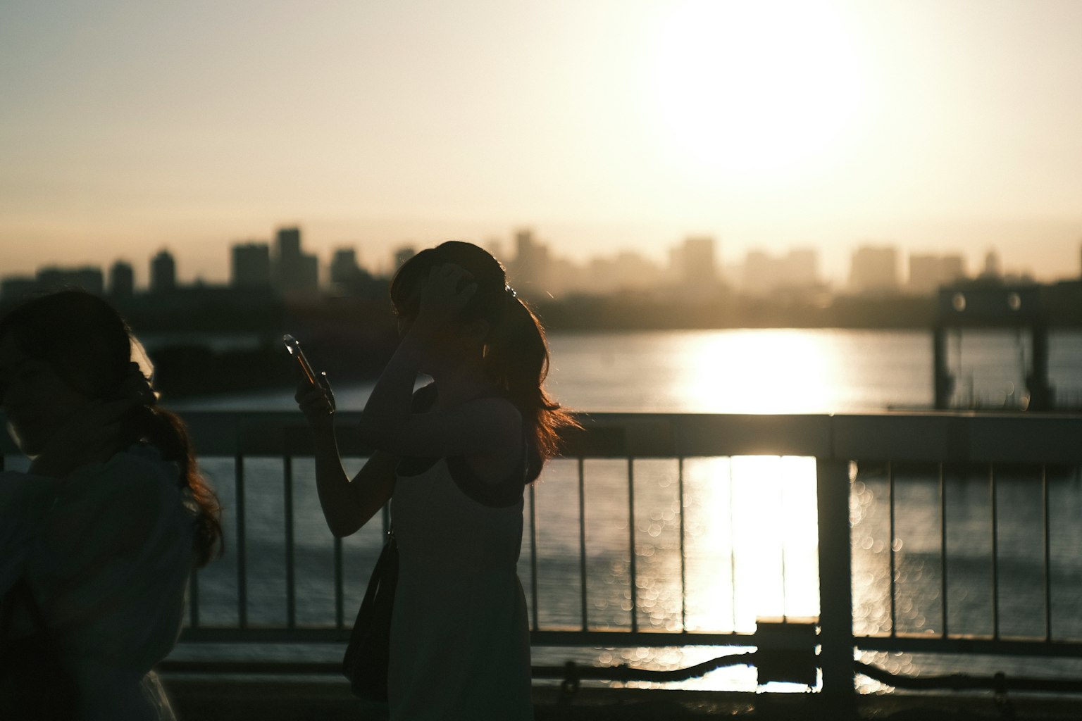 Mujeres en silueta de pie en un puente con un atardecer de fondo