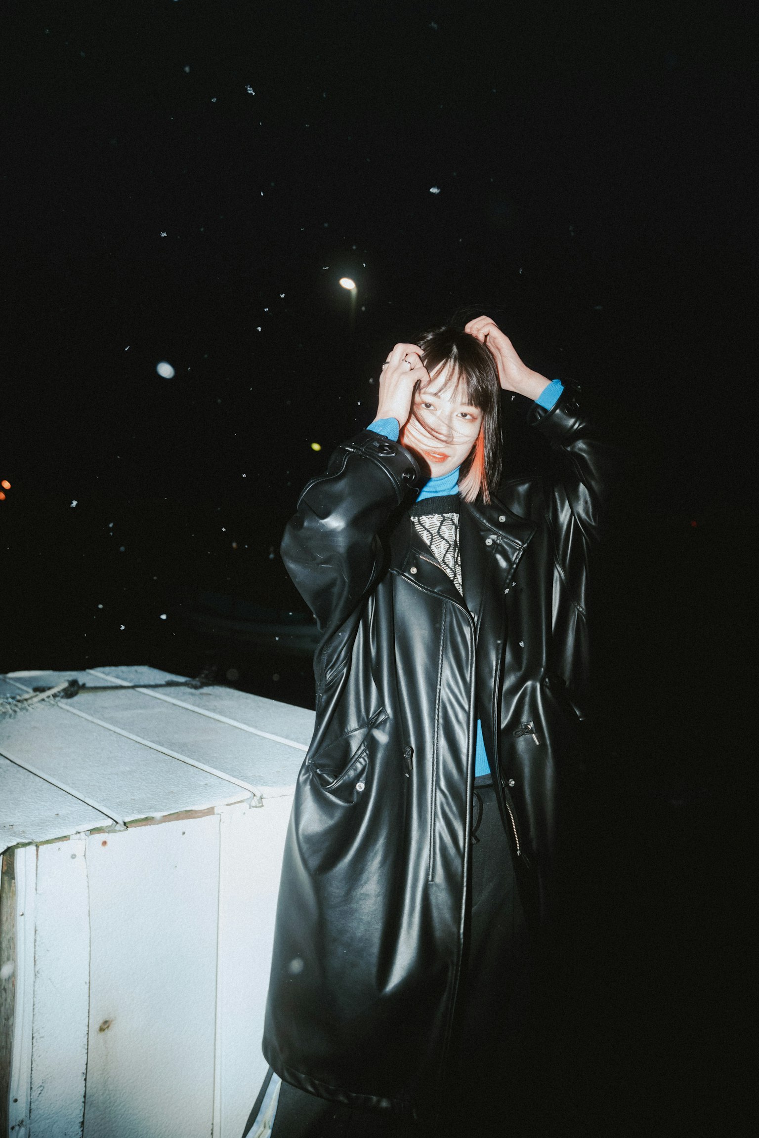 Femme en manteau noir touchant ses cheveux dans une scène nocturne