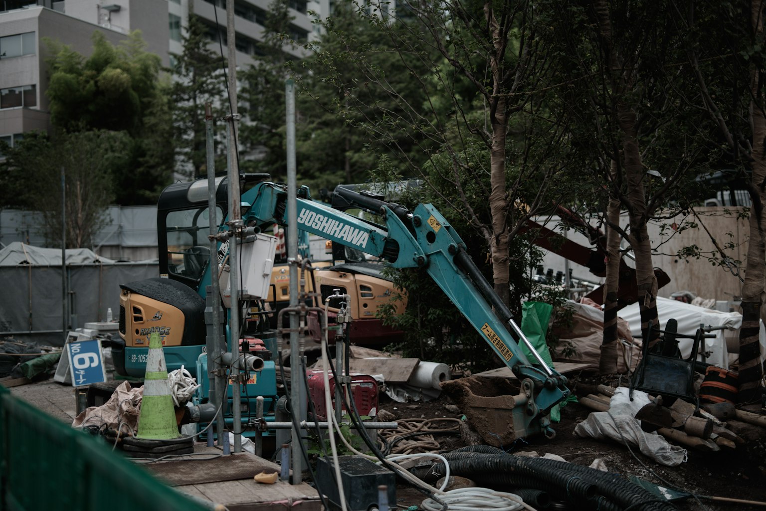 ไซต์ก่อสร้างพร้อมเครื่องจักรและต้นไม้เขียวขจีรอบๆ