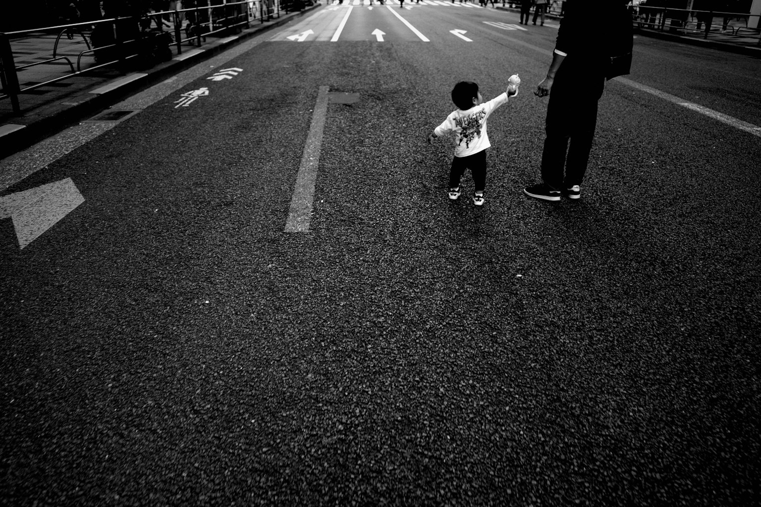 Anak memegang tangan orang dewasa berjalan di jalan hitam dan putih