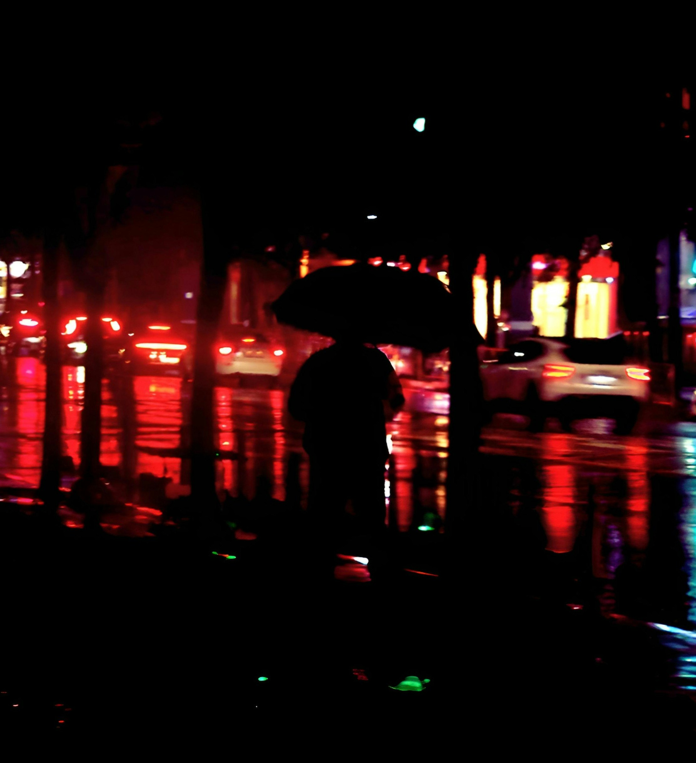雨の夜の街で傘をさす人影のある路地