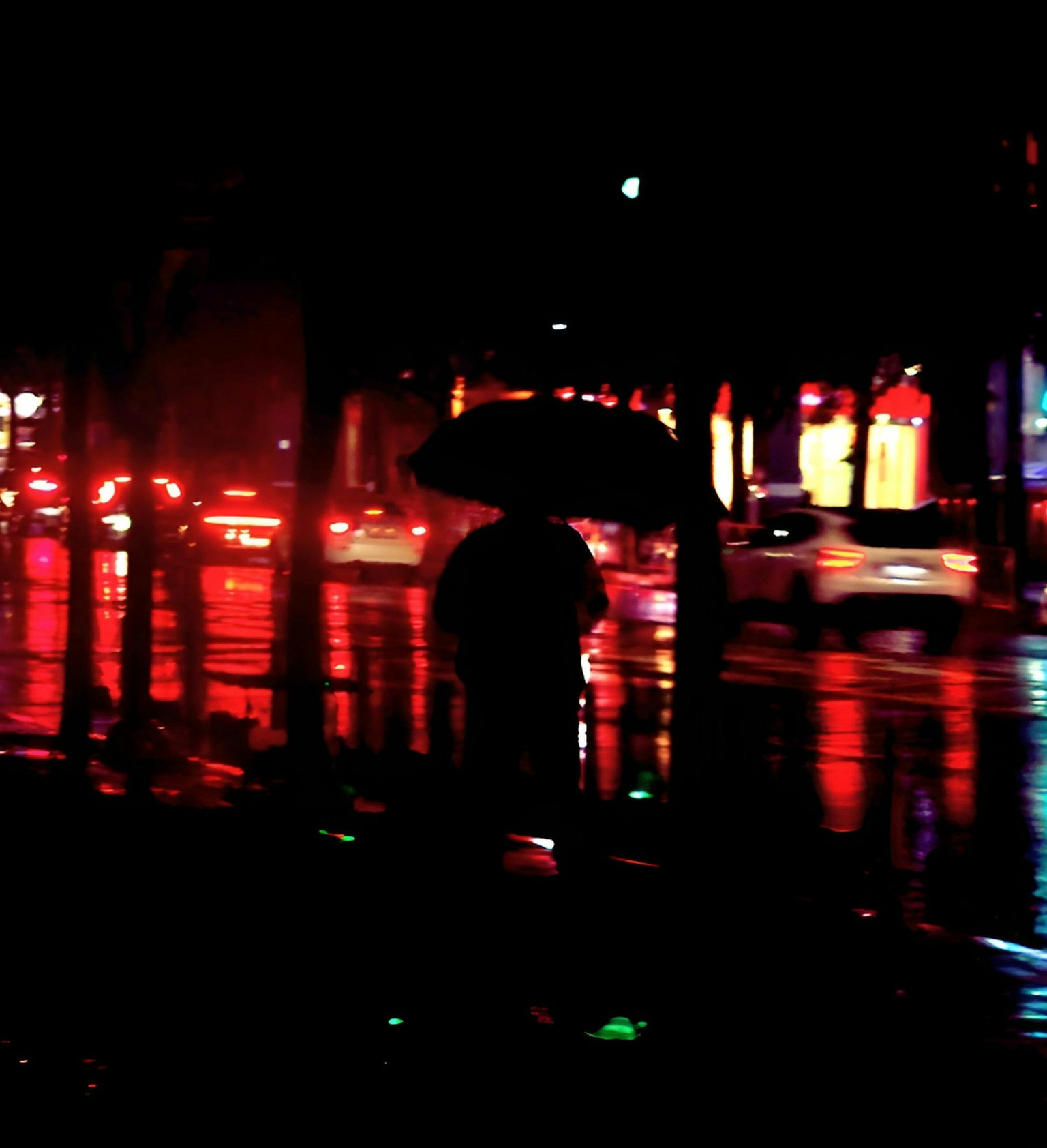 夜の街で傘を持つ人影と反射する光