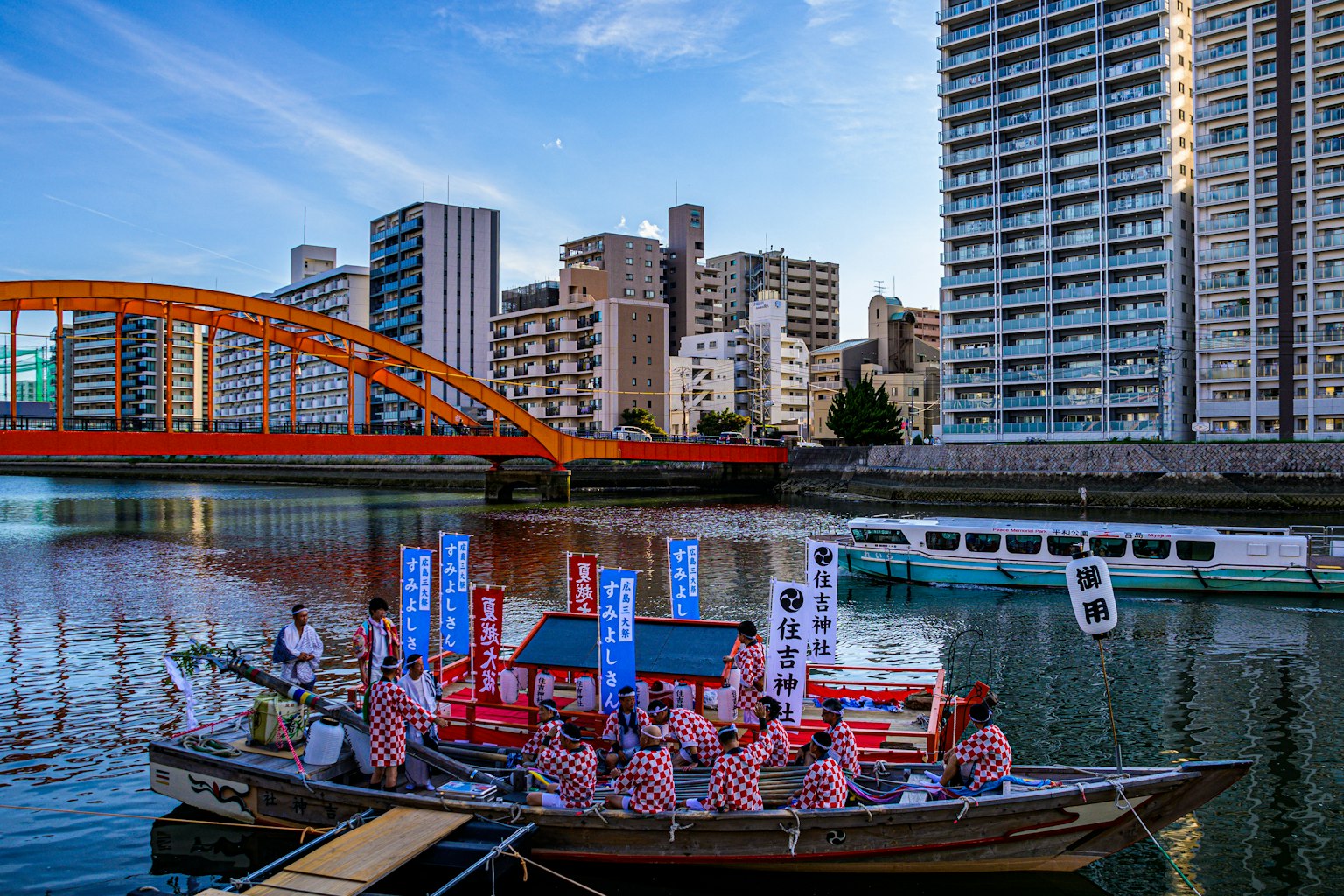 Una vista escénica de personas en un bote en un río con un puente rojo y rascacielos al fondo