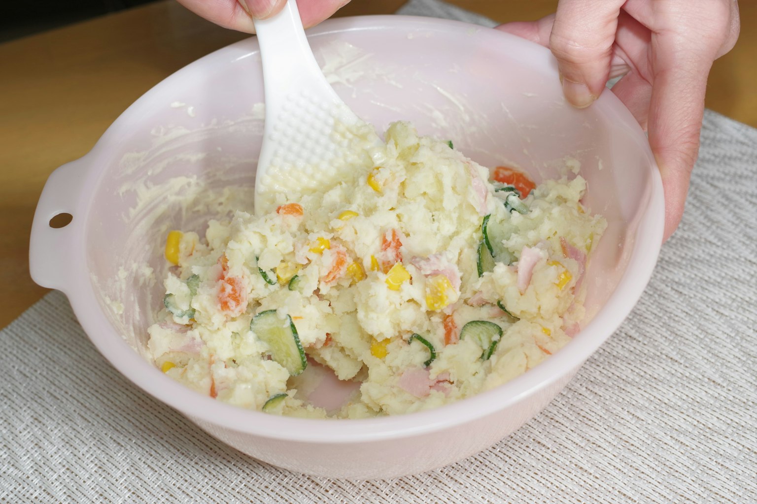 Mixing potato salad in a pink bowl with vegetables