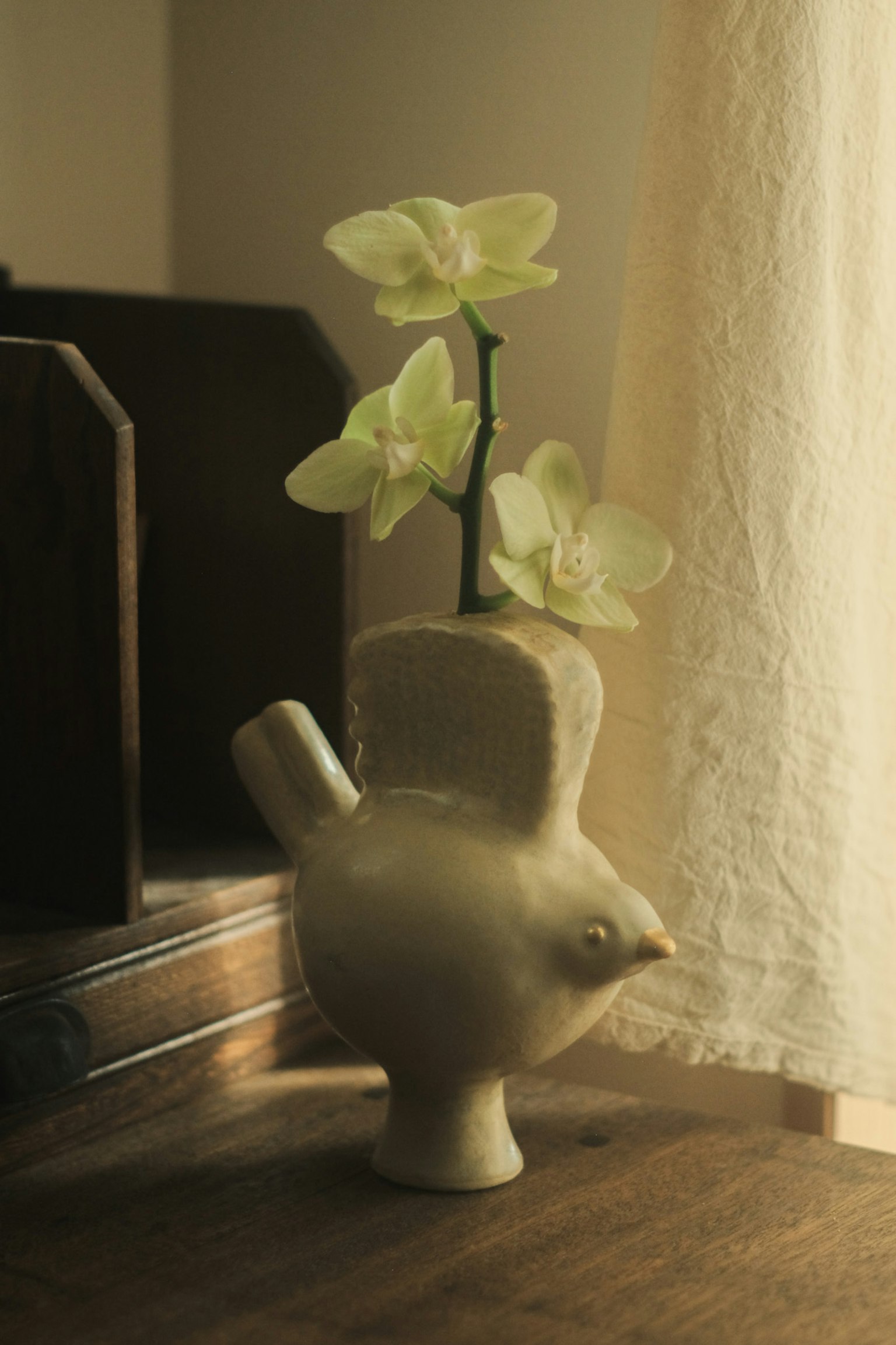 陶器の鳥の花瓶に白い花が生けられているシーン