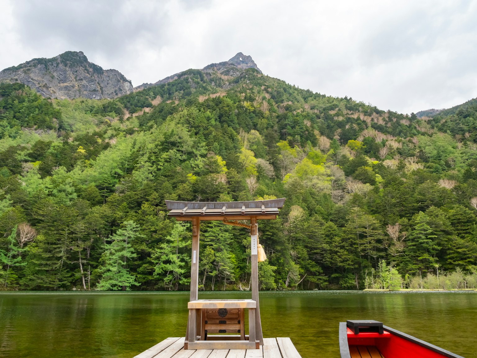 ทิวทัศน์ของทะเลสาบสงบพร้อมท่าเรือไม้เล็ก ๆ ที่ล้อมรอบด้วยภูเขาที่เขียวชอุ่ม