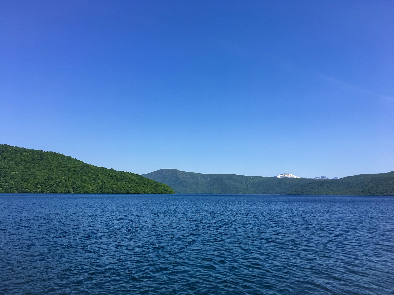 Vista panoramica di un lago calmo circondato da montagne verdi sotto un cielo blu chiaro