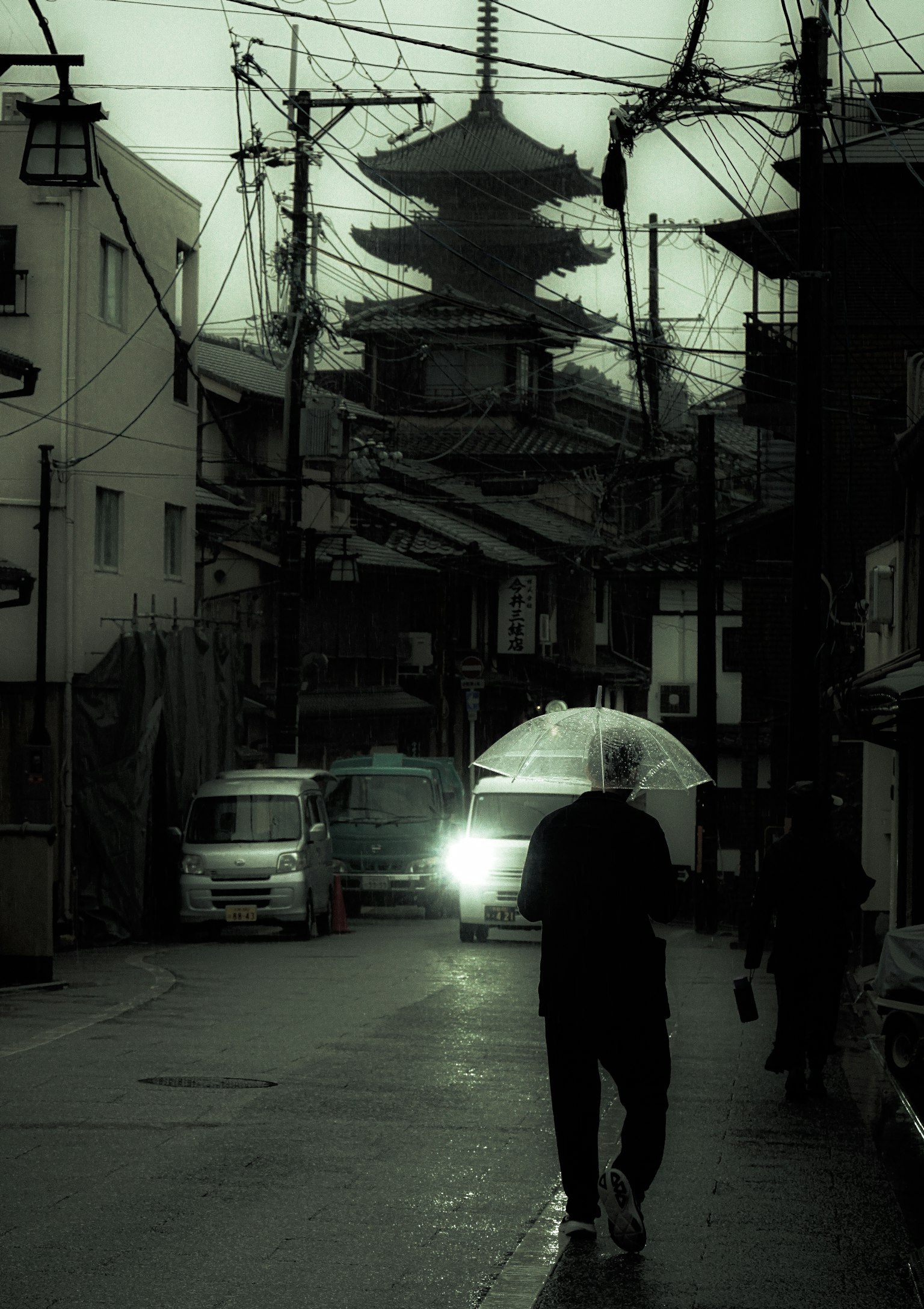 Eine Person, die mit einem Regenschirm auf einer schwach beleuchteten Straße mit einer Pagode im Hintergrund geht