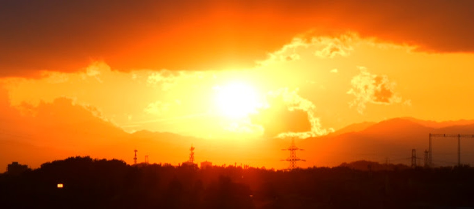 Tramonto che brilla tra le nuvole con montagne e linee elettriche in silhouette
