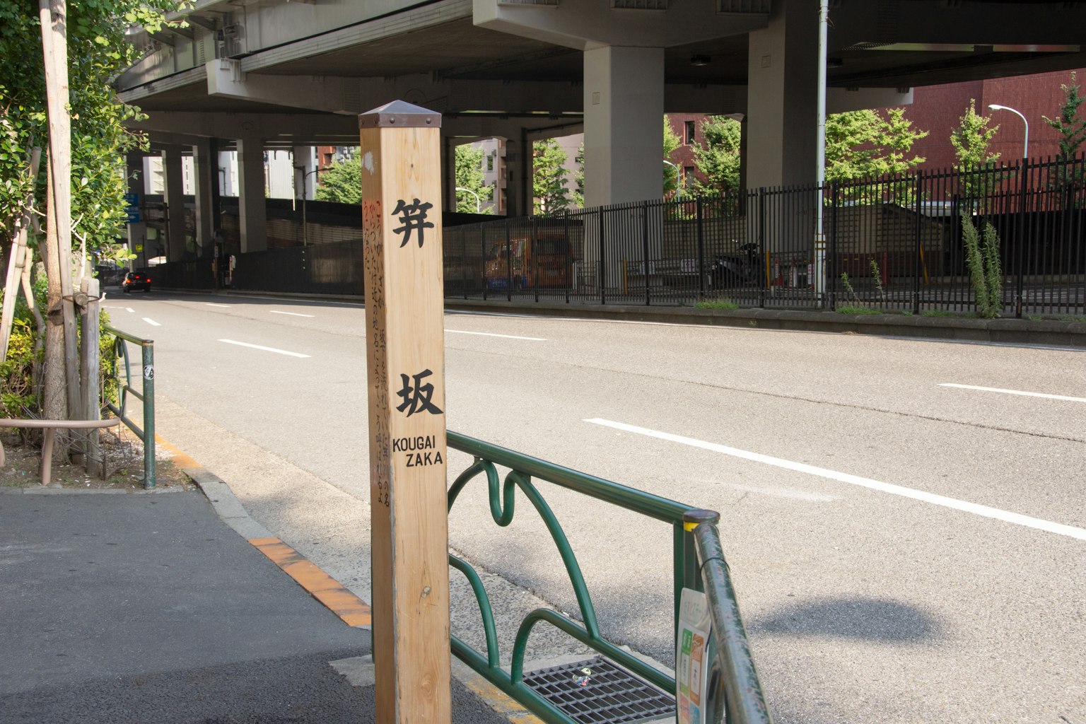 Una scena di strada con un palo di legno che presenta caratteri kanji che indicano un nome di quartiere o strada