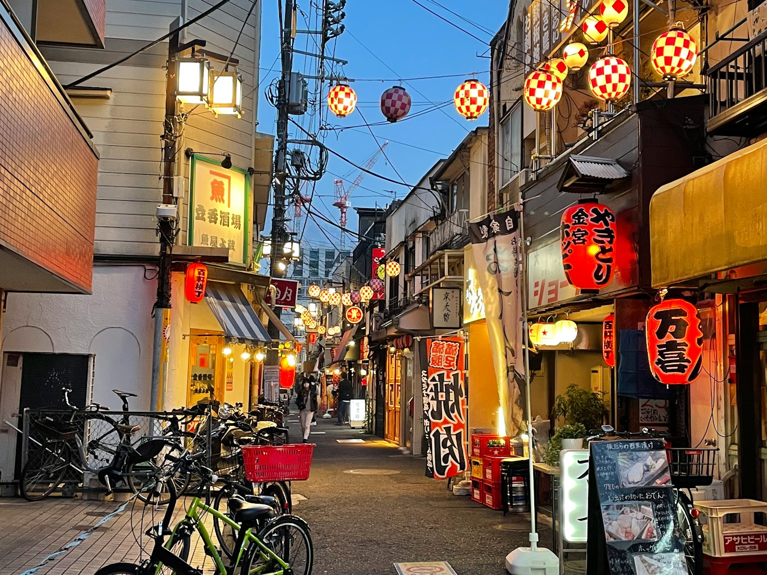 Escena nocturna de una calle comercial japonesa con bicicletas y faroles letreros de restaurantes iluminados