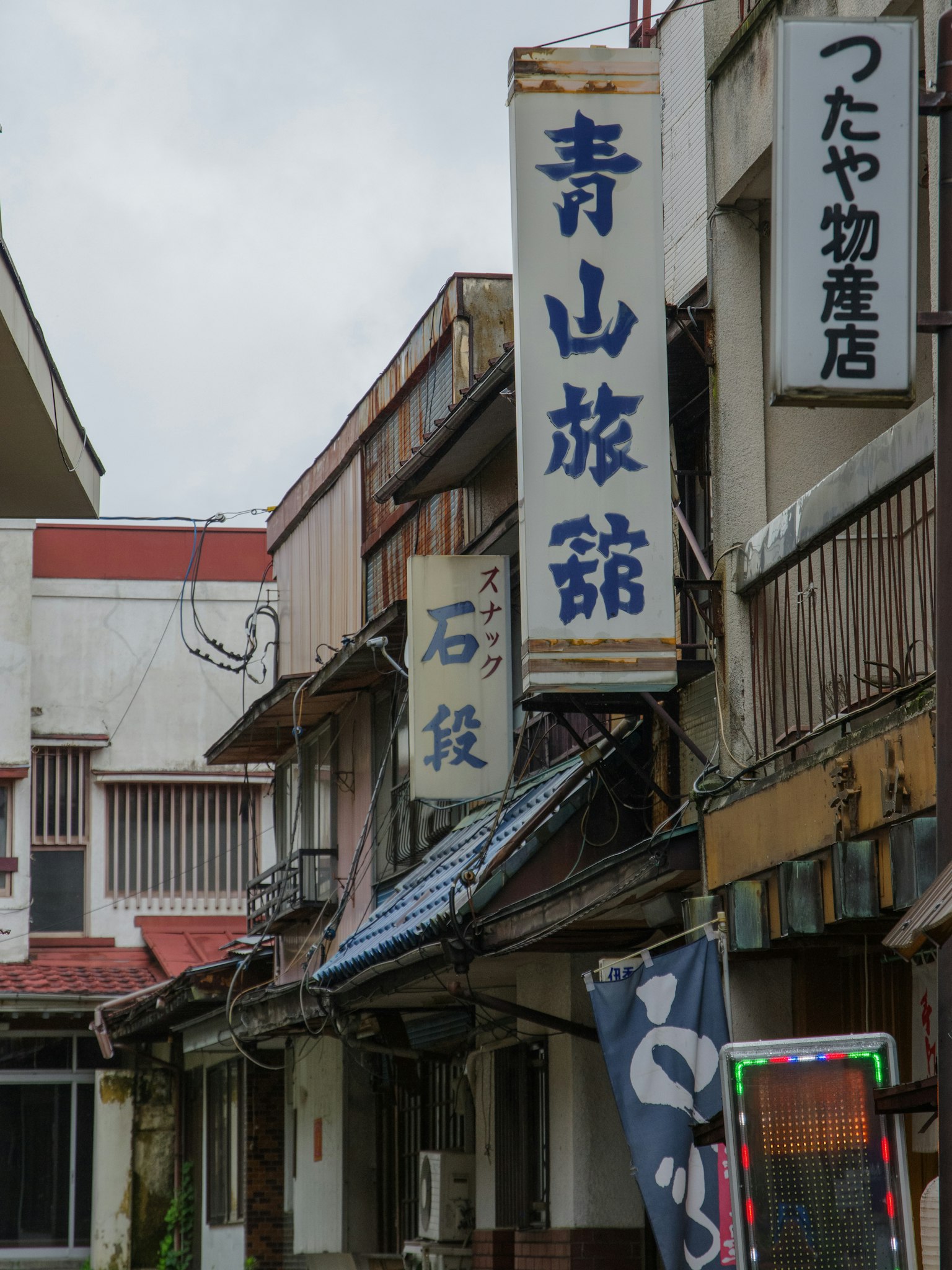 Ansicht einer alten Einkaufsstraße mit Schildern, darunter das Aoyama Ryokan