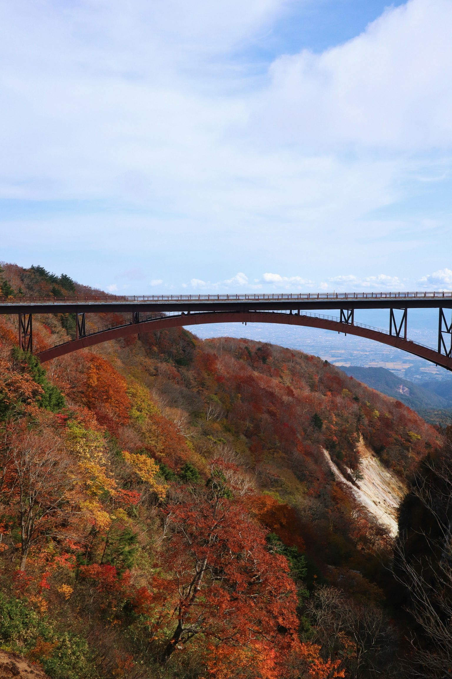 A railway bridge spanning colorful autumn hills and a waterfall