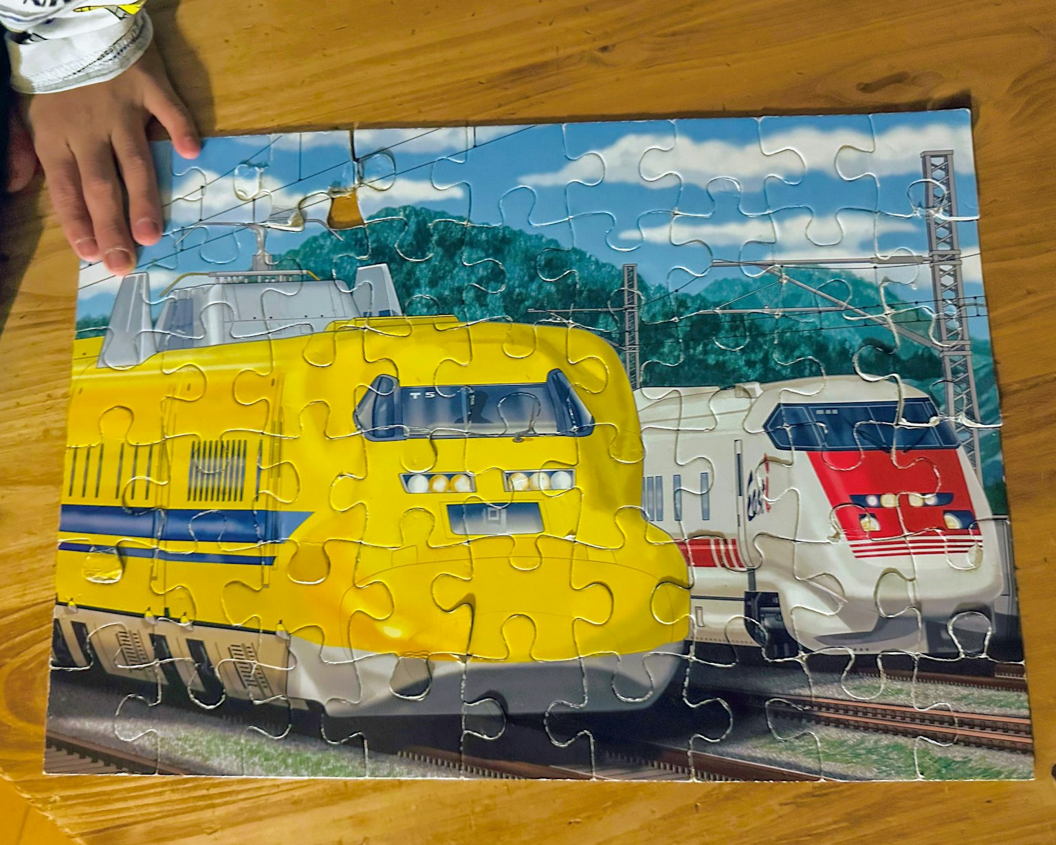 Puzzle complet con un treno giallo e bianco e la mano di un bambino che lo tocca
